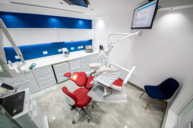 Treatment room with a red dental chair and digital screens